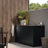 Modern black outdoor kitchen sink with storage. Stainless steel top, wooden fence, lemon plant, small patio.