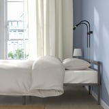 Bedroom scene: a GRIMSBU bed frame under a window, featuring white bedding and pillows. A reading lamp is attached to the headboard.