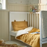 Baby bed with yellow blanket & toys in cosy nursery.