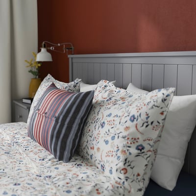 Bedroom with GULLABERG headboard, patterned pillows, striped cushion, and bedside lamp with yellow vase.