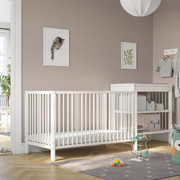 A baby cot in pink nursery with adjustable base & mesh.