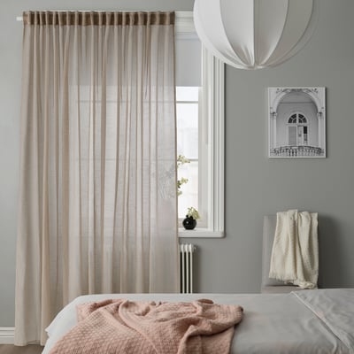 Modern bedroom with beige HÄLLEBRÄCKA curtains, sheer recycled polyester, framing large window beside a cosy bed.