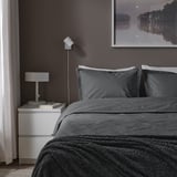 Cosy bedroom with dark grey HAMPFLOCKEL duvet, white bedside table, lamp, book, and lake poster.