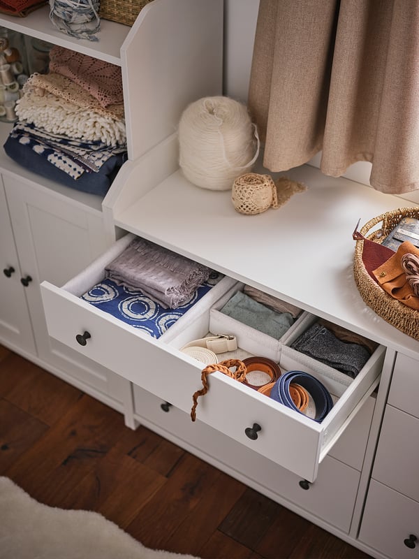 White HAUGA storage unit with multiple compartments, containing yarn, knitting supplies, and linens. Neatly organised with drawers and shelves.
