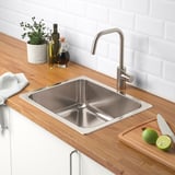 Stainless steel sink with wooden countertop, cutting board, limes, knife, tap, and plant.