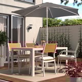 Backyard patio with hogoen grey parasol, white table, and four wooden chairs. Parasol large, providing shade over dining set on brick floor.