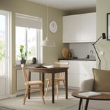 A cosy kitchen with a HÖGVED chair at a table near a window. The chair is light wood, fitting well under the table and beside a large white cabinet.