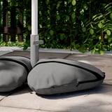 Grey IGGÖN sandbags for parasol, made of recycled polyester, with black trim, placed outdoors on concrete.