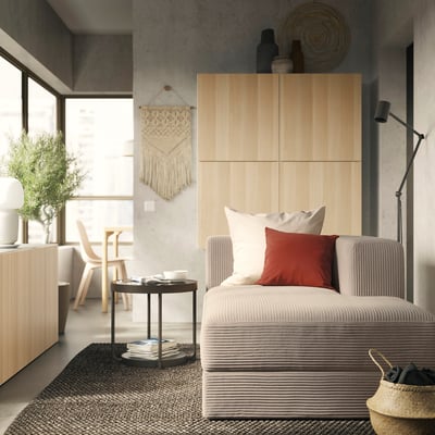 Modern living room with light wooden cabinets, a grey striped sofa, red pillow, wicker basket, and hanging wall decoration.