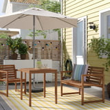 Outdoor patio with beige JOGGESÖ parasol, wooden table, and chairs on striped yellow rug.