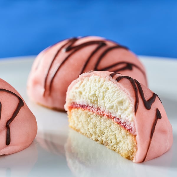 Three creamy pink pastries, one cut open revealing raspberry filling and whipped cream. Smooth icing, fluffy filling, crisp base.