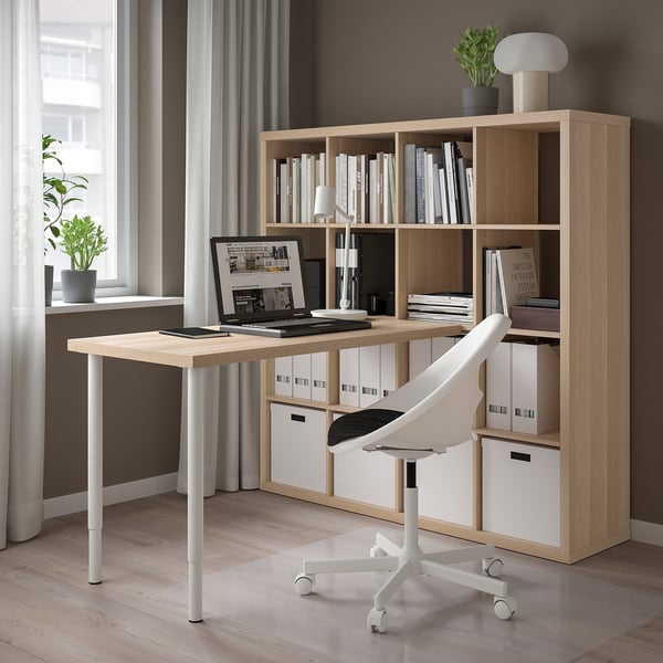 Minimalist office setup with KALLAX oak shelving, white desk, and chair. Laptop on desk by window.