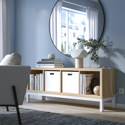 Minimalist living room with blue walls, grey chair, KALLAX shelves with books, vases, and a large mirror.