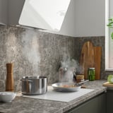 Modern kitchen with marble countertop, induction hob, pots, pepper grinder, and range hood.