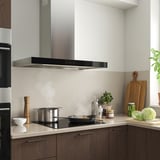 Modern kitchen with stainless-steel range hood, wooden cabinets, and utensils. Hood has touch controls and led lighting.