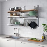 Professional-style kitchen organiser. Metal and wood shelves, stainless steel details. Holds bowls, platters, and glasses. Mounted above the sink.