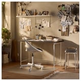 Creative workspace with white desk, chair, and stool. Decorated with art, plants, and books. Light-filled and cosy.