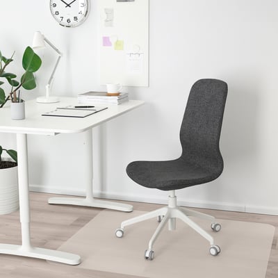 Minimalist home office with black LÅNGFJÄLL chair, desk, books, lamp, and clock.