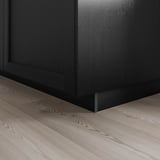 Black kitchen cabinet base with bevelled edges on light wooden floor, showing robust, traditional design.