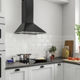Modern kitchen with large black range hood, white cabinets, black countertop, and stainless steel appliances.
