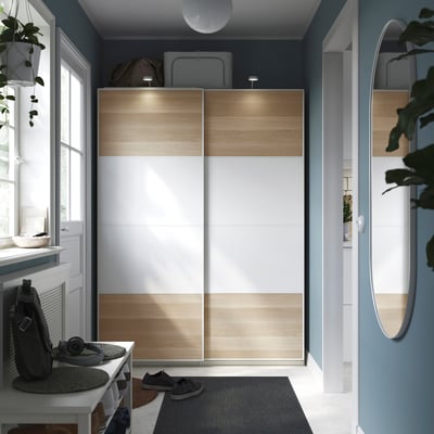 Modern closet with sliding doors, featuring light wood and white panels. Well-organized entryway with stylish decor.