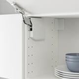 Kitchen cabinet hinge detail, showing adjustable metal arm and white cabinet frame with drilled holes.