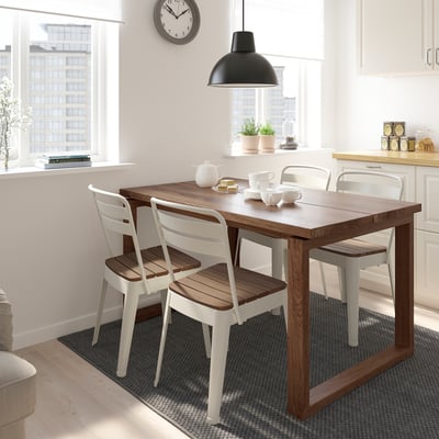 Small dining set with wooden table and white chairs, positioned near a kitchen window with a city view.