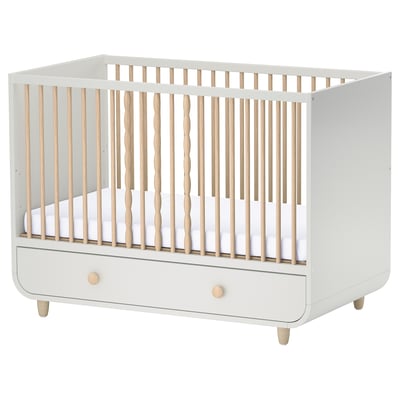 A MYLLRA white and light wood baby crib with one removable side and a drawer at the base.