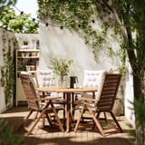 Outdoor patio with acacia wood NÄMMARÖ table and chairs, white cushions, hanging lights, and plants.