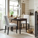 Cosy dining nook with dark table, light grey chairs, plants, and rug. Brightened by window and pendant light.