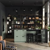 Modern kitchen with green drawers, open shelves displaying items, and minimalist black bar stools.