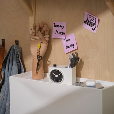 Small white alarm clock with pen storage, keys, sticky notes, pen holder, earbuds.