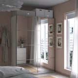 Modern bedroom with PAX wardrobe, sliding mirror doors, grey linens, white decor, and natural light from a large window.