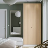 Minimalist bedroom with large light wooden PAX wardrobe, tall mirror, and white decor.