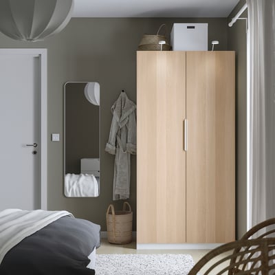Minimalist bedroom with PAX wardrobe, mirror, bed, baskets, lamp, and curtains.