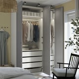 Open wardrobe with clothes, drawers, and plant.