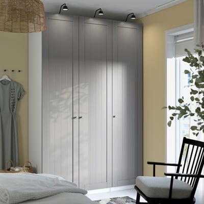 Minimalist closet, tall black chair near window, grey PAX wardrobe and grey bed, light yellow walls.