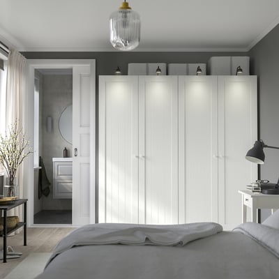 Modern bedroom with white PAX wardrobe, built-in lights, grey bed, bedside table, and adjacent bathroom.