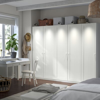 PAX wardrobe dominates room, tall and wide with multiple compartments. Storage boxes atop, desk below window, bed beside.