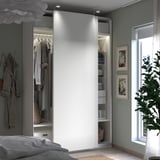 Modern bedroom with white PAX wardrobe, clothes, shelves, light grey walls, white bed, green plant.