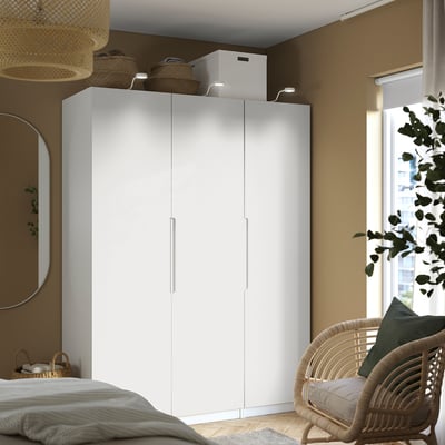 Minimalist white PAX wardrobe dominates room. Tall, sleek, houses wicker chair right. Topped with woven baskets, mirror left.