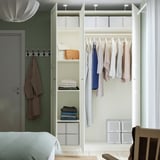 Modern closet organising clothes, with hanging shelves and lit upper section, in a minimalist bedroom.