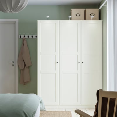 White wardrobe by doorway, boxes on top, coat on hooks, blue bed, wooden chair.