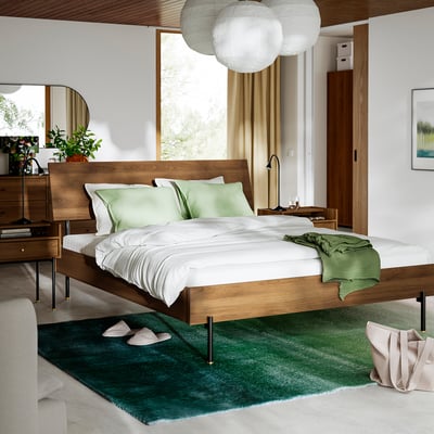 Minimalist bedroom with RÅDMANSÖ bed & bedside table, large bed, white sheets, green throw, globe lights, rug, slippers.