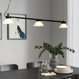 Modern dining scene with SAMBORD pendant lamp, three shades, illuminating table, plates, glasses, and vase with greenery.