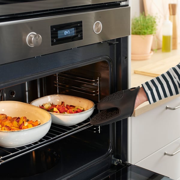 Person using oven mitt to remove dishes from oven. The mitt protects hands and provides a firm grip.