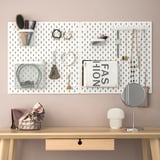 SKÅDIS pegboard organises jewellery and accessories with hooks, bags, mirror, and lamp on table.