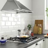 Modern kitchen with SKÅLAN gas hob, dark counter, light backsplash, range hood, and cooking items.