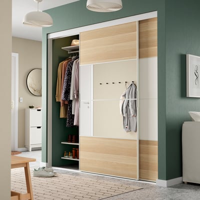 SKYTTA wardrobe: green & beige, mirrored sliding doors, wooden panels. Its large, taller than the white radiator, spacious inside.