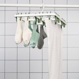A drying rack hangs socks and underwear with clips against a tiled wall.
